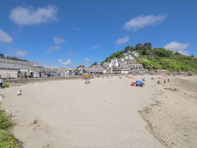 A beach with people and houses on a hill at Mayhurst in Looe