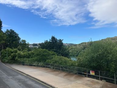 A view from a road with trees and a body of water at Mayhurst, Looe