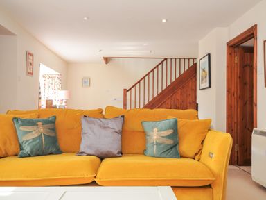 A living room with a yellow sofa and decorative pillows at Rosewin Farmhouse near St Minver