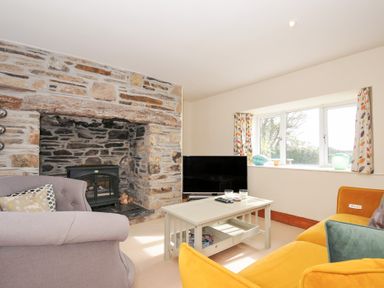 A living room with a fireplace and a television at Rosewin Farmhouse near St Minver