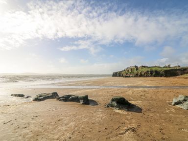A beach with sand and rocks near a cliff and buildings at Dunbrody Dreams