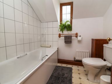 A bathroom with a bathtub, toilet, and window at Denhill Cottage