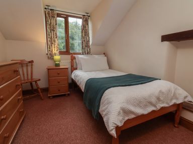 A bedroom with a single bed and wooden furniture at Denhill Cottage