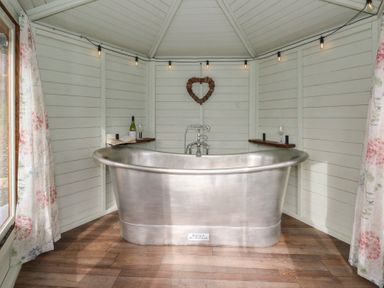 A bathroom with a silver bathtub and wine bottle on a shelf at Y Cwlwm in Lampeter