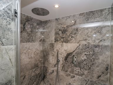 A shower with stone tiles and showerhead at The Boundary in Windermere