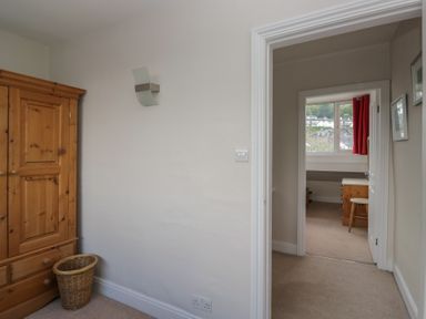 A bedroom with a wardrobe, basket, and doorway to another room at Cloud Cottage Ambleside