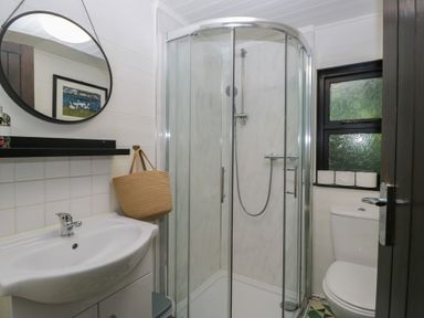 A bathroom with a shower, sink, toilet, and mirror at Moon Cottage near White Cross Bay Holiday Park