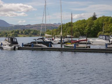 Boats docked at a marina with mountains in the background at Moon Cottage White Cross Bay Holiday Park near Troutbeck Bridge