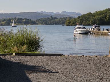 A waterfront scene with boats and a man on a paddleboard at Moon Cottage near White Cross Bay Holiday Park near Troutbeck Bridge