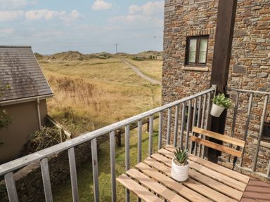 A balcony with a table and chairs overlooking a grassy area at Awel y Môr in Burry Port