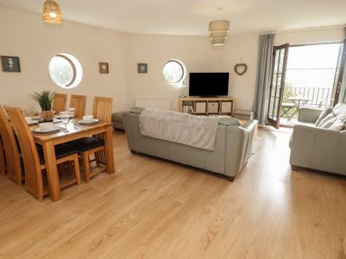 A living room with a dining table and chairs, sofa, and television at Awel y Môr, Burry Port