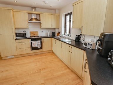 A kitchen with cabinets, stove, sink, microwave, kettle, and radio at Awel y Môr Burry Port