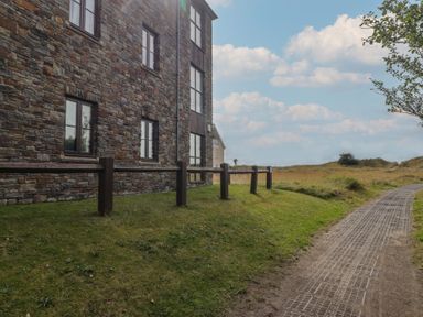 An outdoor view of a stone building and a pathway at Awel y Môr in Burry Port