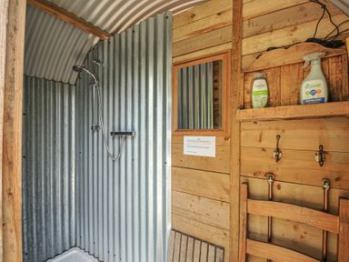 A shower with striped metal wall and wooden elements at Prudence in Panson Mill near Ashwater