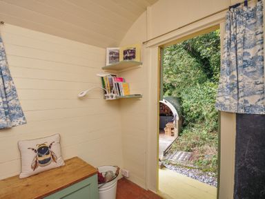 A small room with a bench, shelves, and a door leading outside at Prudence in Panson Mill near Ashwater