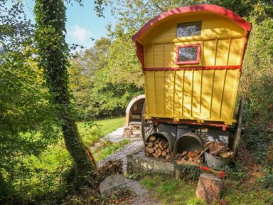 A yellow caravan with wood storage and outdoor seating at Prudence, Panson Mill near Ashwater