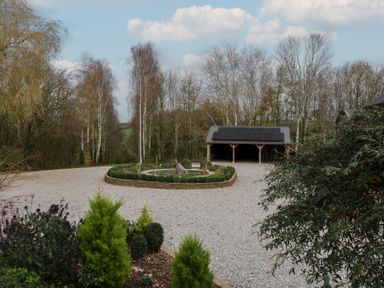 A gravel driveway with a round stone planter and seating area at a 3 bed property