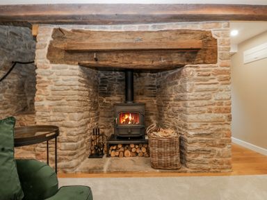 A fireplace with a wood stove and a basket of logs in a living room at 1 bed property Usk