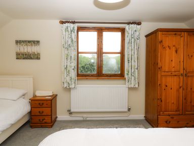 A bedroom with a bed, nightstand, wardrobe, and window at The Milking Shippon at Thorne, Langtree near Great Torrington