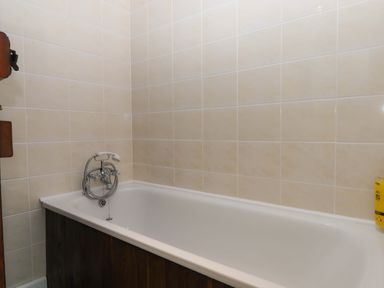 A bathroom with a bathtub and wall tiles at The Milking Shippon at Thorne, Langtree near Great Torrington
