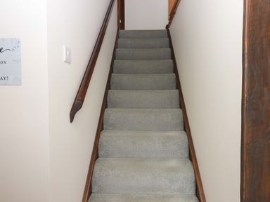 A staircase with grey carpet and wooden handrail at The Milking Shippon at Thorne in Langtree near Great Torrington