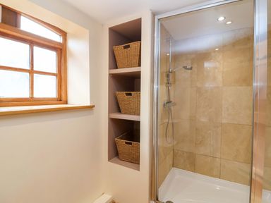 A bathroom with a shower and storage shelves at Millbarn in Crowcombe