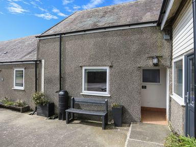 An outdoor view of a building entrance with a bench and plants at Towyn - 7 Ty'n Don