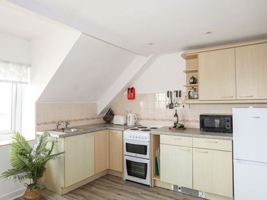 A kitchen with cabinets, stove, microwave and sink at Towyn - 7 Ty'n Don