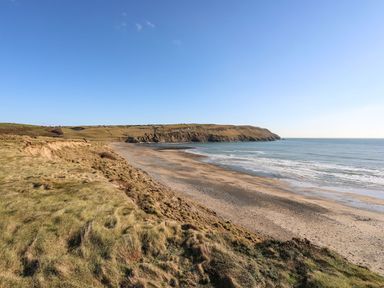 A beach with grass and cliffs along the shoreline at Towyn - 7 Ty'n Don
