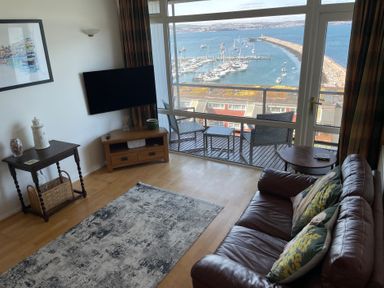 A living room with a television and furniture overlooking the harbor at Snowy Owl View at The Breakwater in Brixham