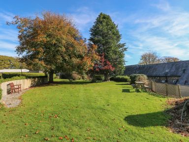 A garden with trees and benches at Knap Cottage in Clarbeston Road