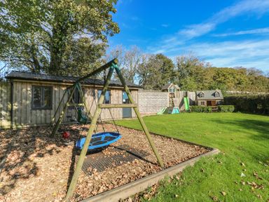 A garden with a swing set and playhouse at Knap Cottage in Clarbeston Road