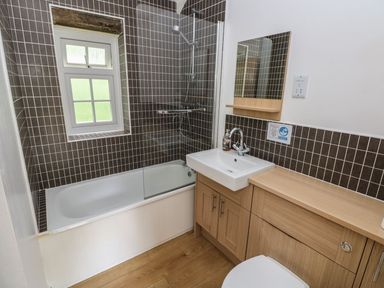 A bathroom with a bathtub, shower, sink, and mirror at Corner Cottage in Clarbeston Road