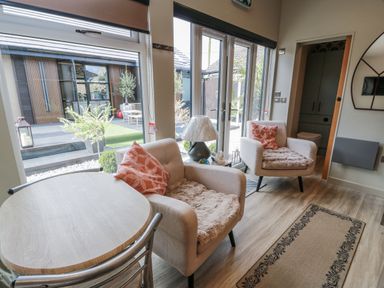 A living room with a table and chairs next to large windows at Cabin At The Brig Annan