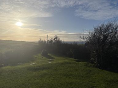 A garden with grass and bushes under a sunset at Harbour Lights Church Bay