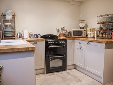 A kitchen with stove, microwave, and shelves at The Old Post Box in Halesworth