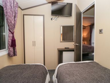 A bedroom with two beds, a wardrobe, and a television at Feather Hill Lodge in Windermere