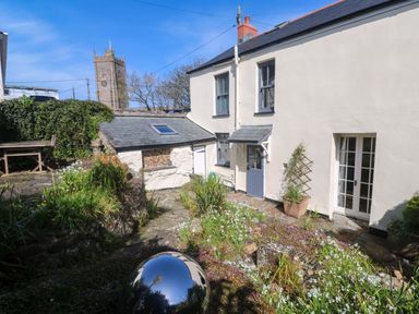 An outdoor garden with a house corner and view of a church tower at Pedn Brose near Mousehole
