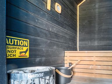 A sauna with wooden bench, stone heater and warning sign at Manor Farm House in Merton near Bicester