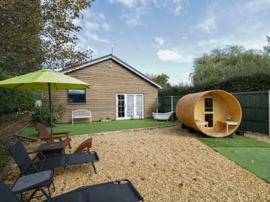 A garden with a wooden building, sauna, and seating at Willow Cottage in Whiteparish