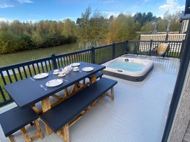 An outdoor dining area with a hot tub by a water view at Lakewood Retreat in Woodhall Spa