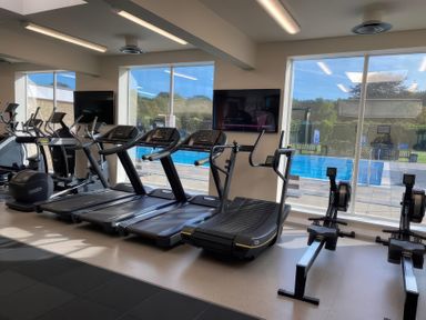 A gym with exercise equipment and windows overlooking a pool at Lakewood Retreat in Woodhall Spa