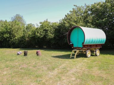 A caravan on grass with a stool and pot at The Bowtop Gypsy Caravan in Eye