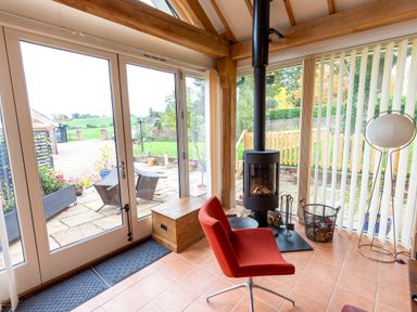 A conservatory with a wood stove and red chair at Nature's Lodge in Cookley
