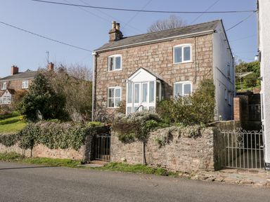 A stone house with white framed windows and a front porch behind a low stone wall with greenery at Gordons View Pleasant Stile near Gloucester