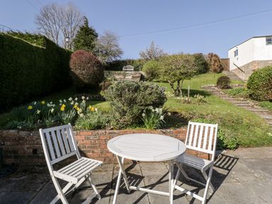 An outdoor patio with a round white table and two white chairs facing a garden with daffodils and a grassy hill at Gordons View Pleasant Stile near Gloucester