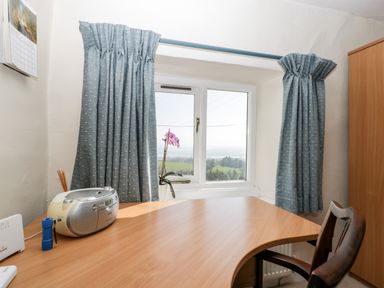 A wooden desk with a radio, blue flashlight, and a chair near a window with blue curtains at Gordons View Pleasant Stile near Gloucester