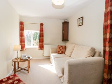 A sitting room with a beige sofa a round wooden table with tea set and lamp and orange patterned curtains at Gordons View Pleasant Stile near Gloucester