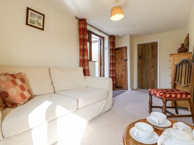A sitting room with a beige sofa, a wooden chair with red patterned cushion, a round wooden table with teacups and teapot, red curtains, and wooden doors at Gordons View Pleasant Stile near Gloucester