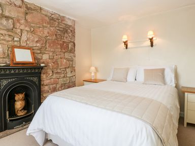 A bedroom with a bed white and beige bedding two wall lamps two bedside tables and a stone wall with a fireplace at Gordons View Pleasant Stile near Gloucester